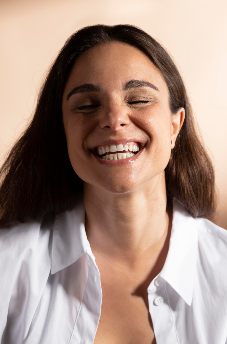 Woman smiling with her eyes closed, wearing a white shirt, on a light background