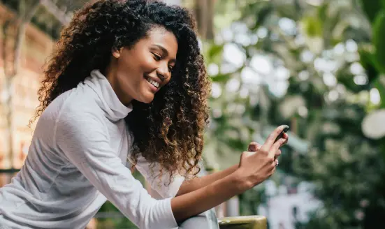 A woman with curly hair smiling while looking at her phone